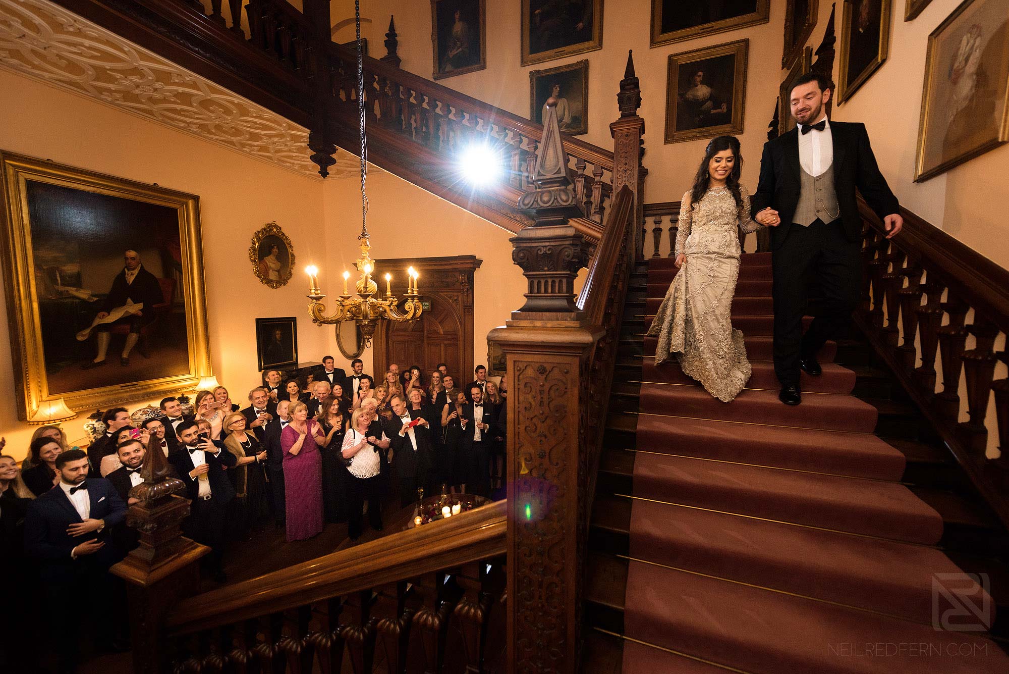 bride and groom walking down stairs at Arley Hall in front of friends and family