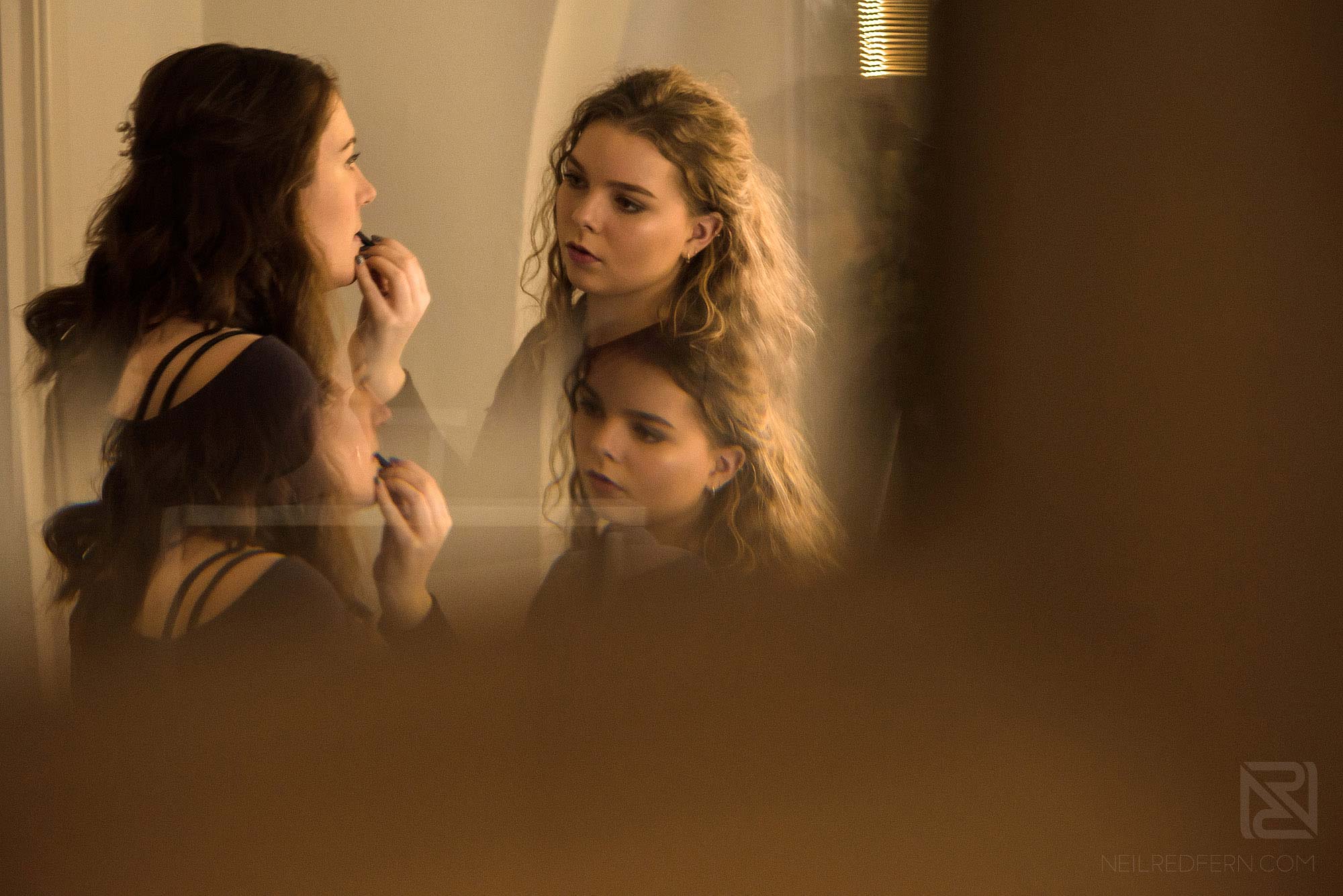 reflection in mirror of bridesmaid having lipstick put on 