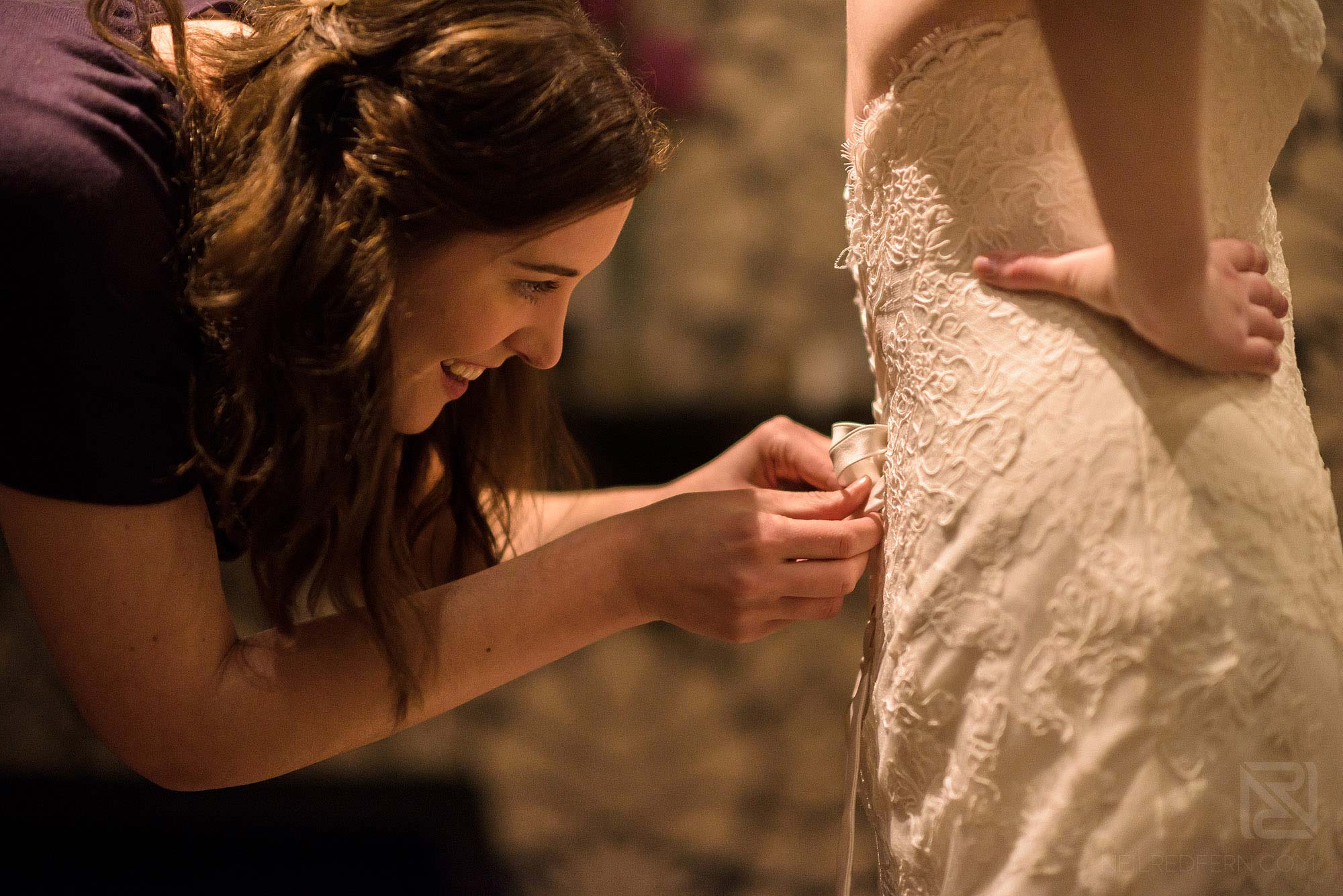 bridesmaid helping bride get in to wedding dress