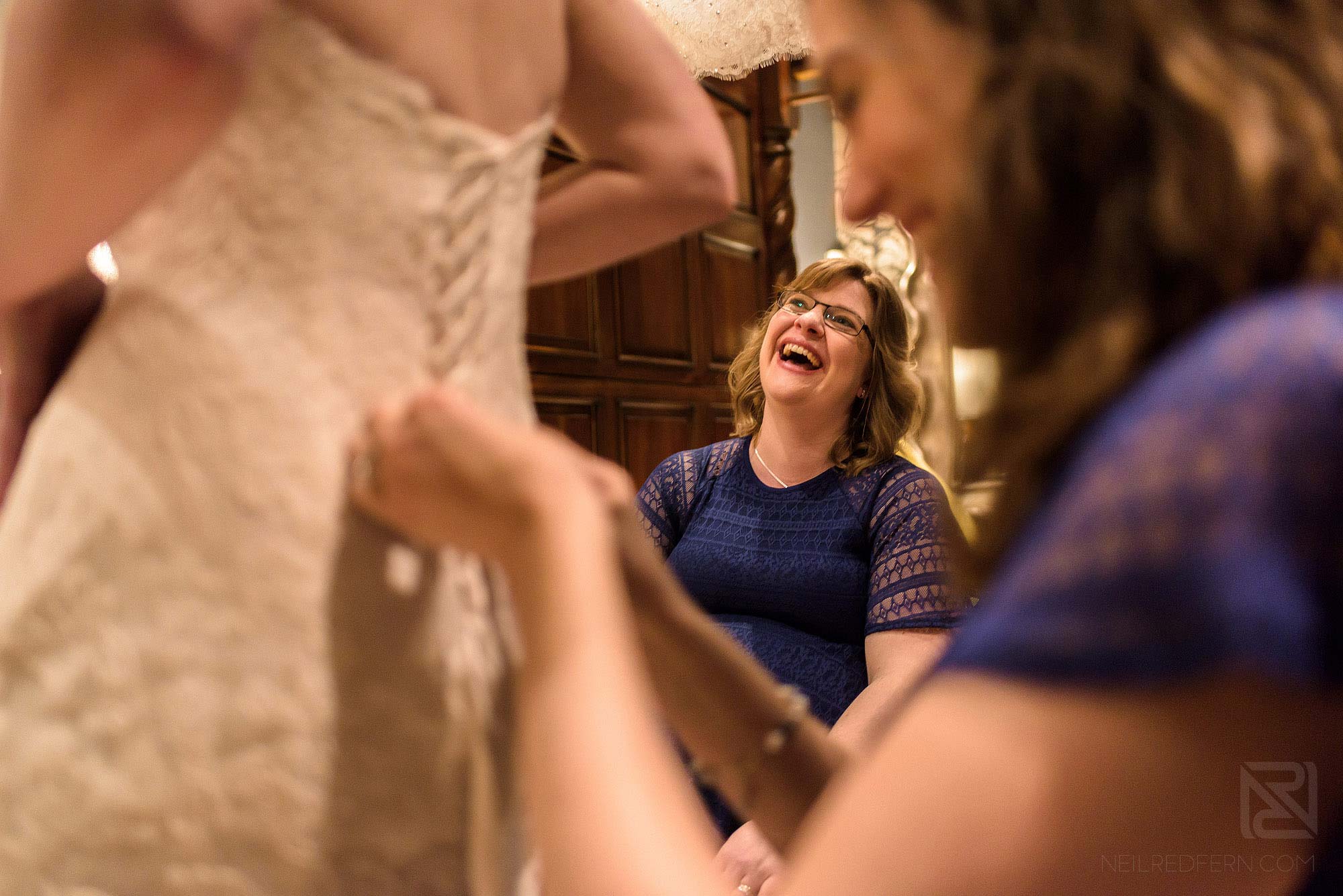 bridesmaids laughing whilst doing up back of bride's wedding dress