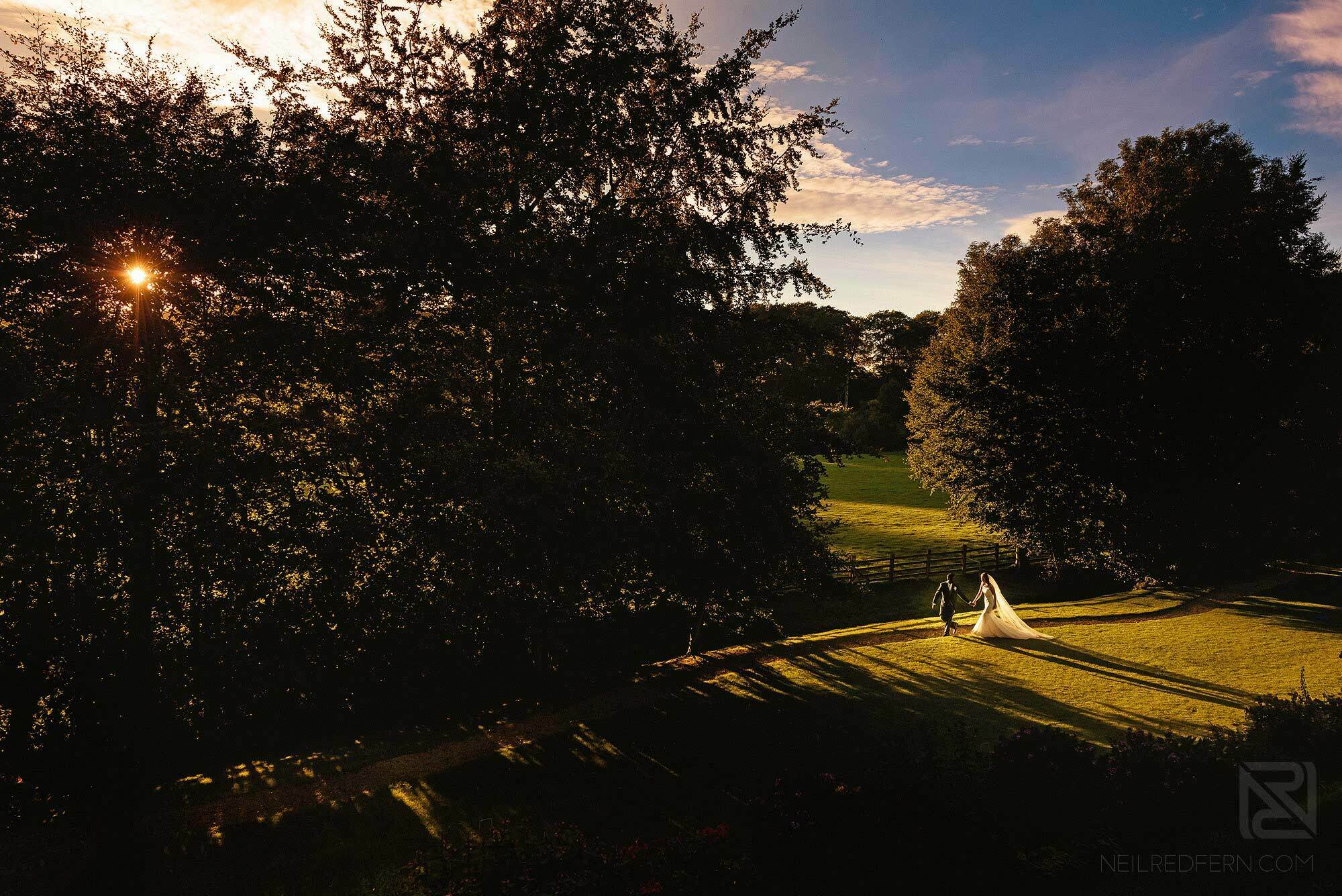 wide angle photograph of bride and groom walking through gardens at Mitton Hall in Lancashire