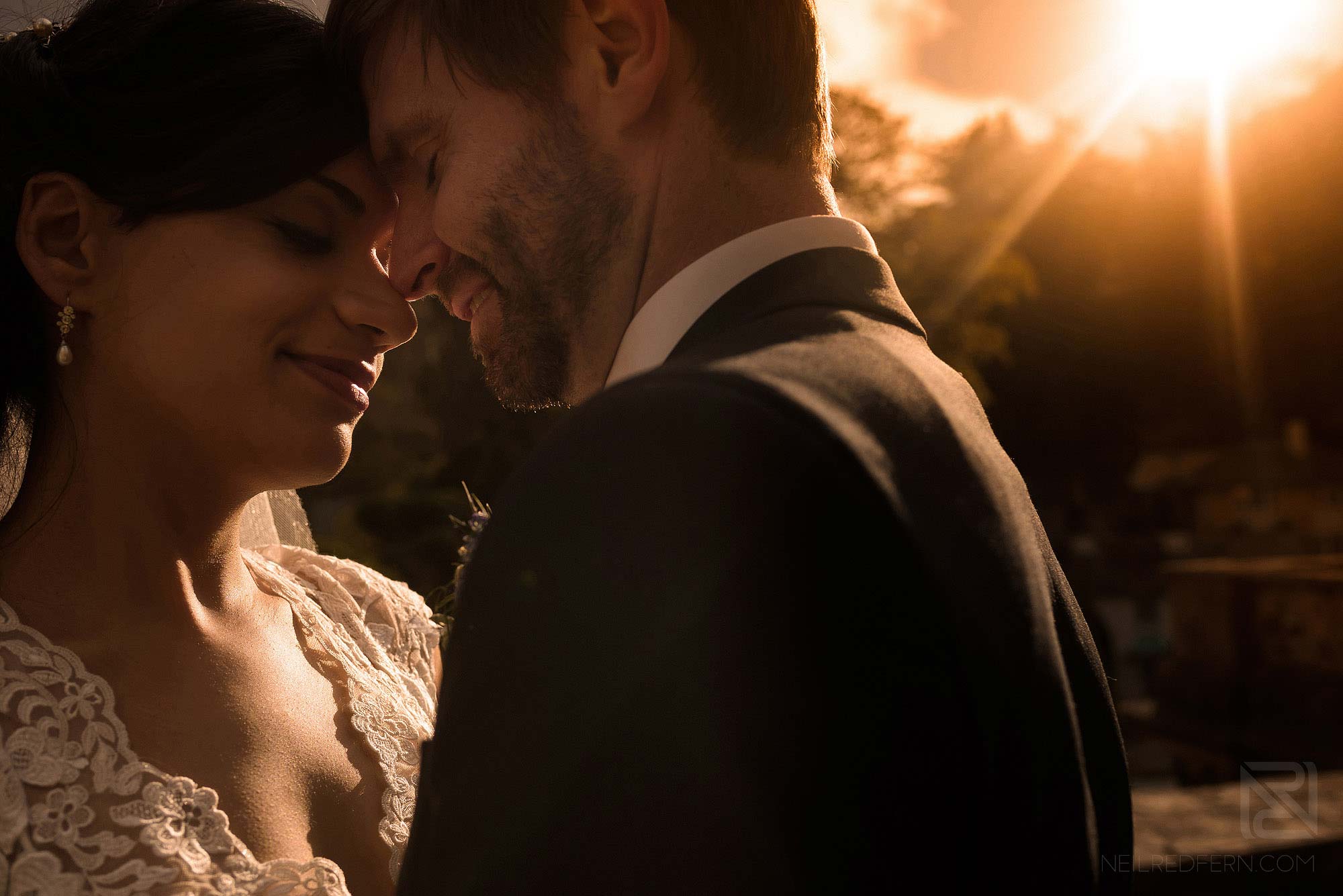 close up photograph of bride and groom with sun going down behind them