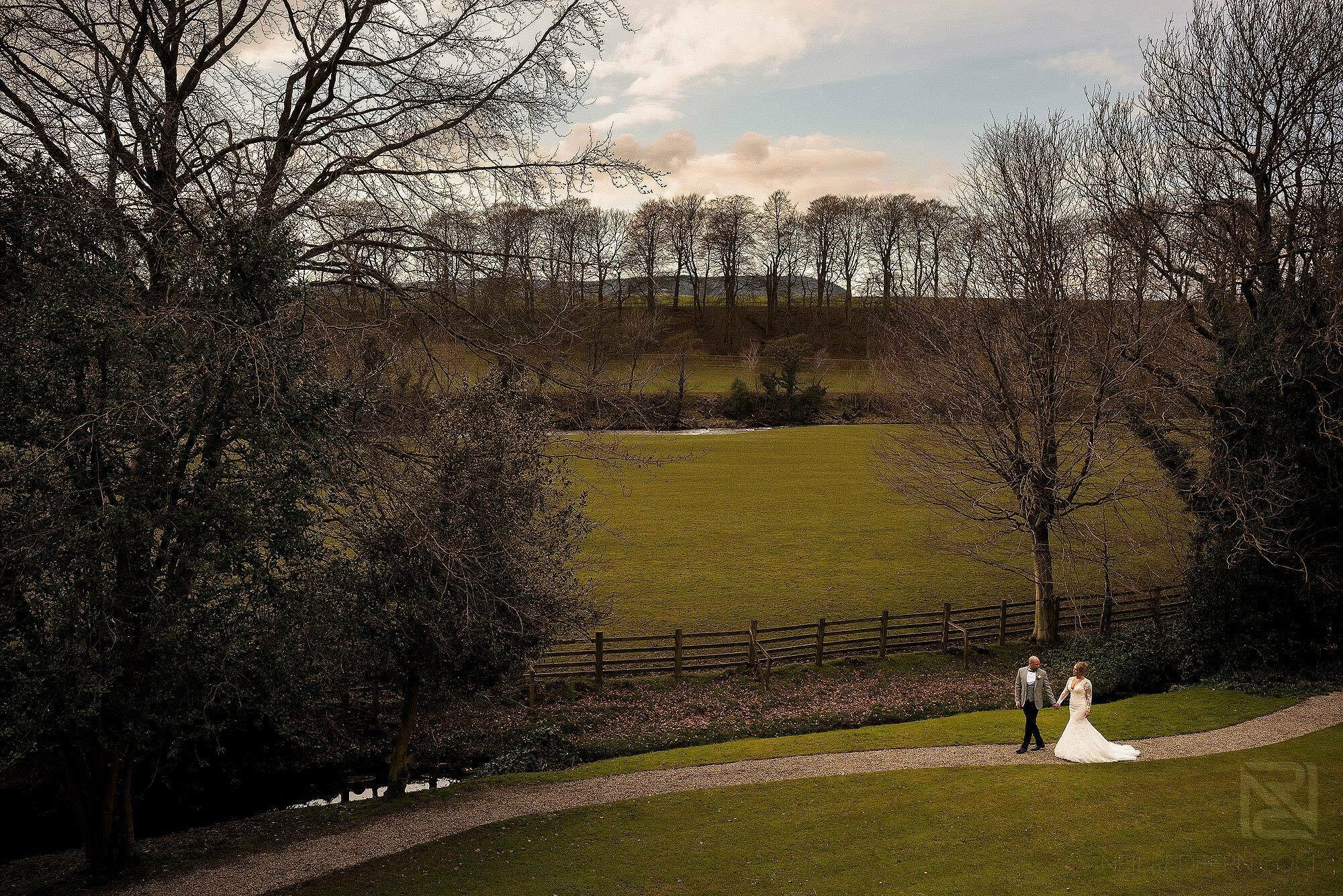 wide angle photograph of happy bride and groom walking through the gardens at Mitton Hall