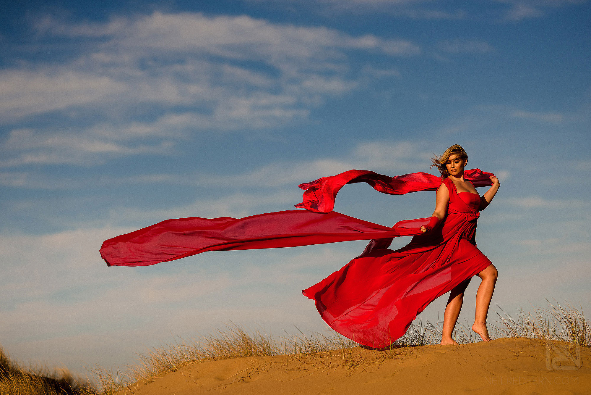 photograph of bride with long red dress blowing in the wind