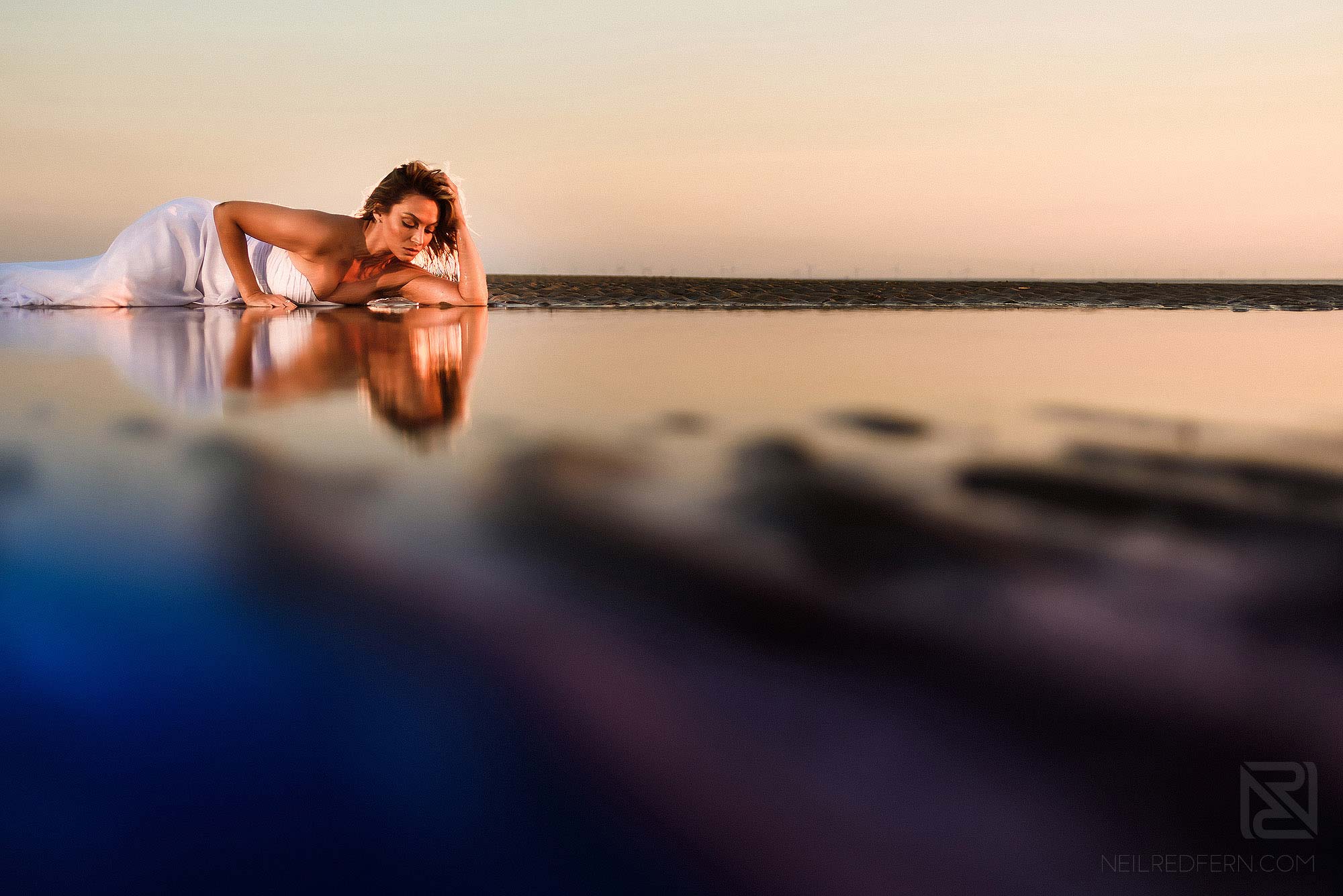 Trash the dress shoot on the beach 6 reflection of bride lying next to the water