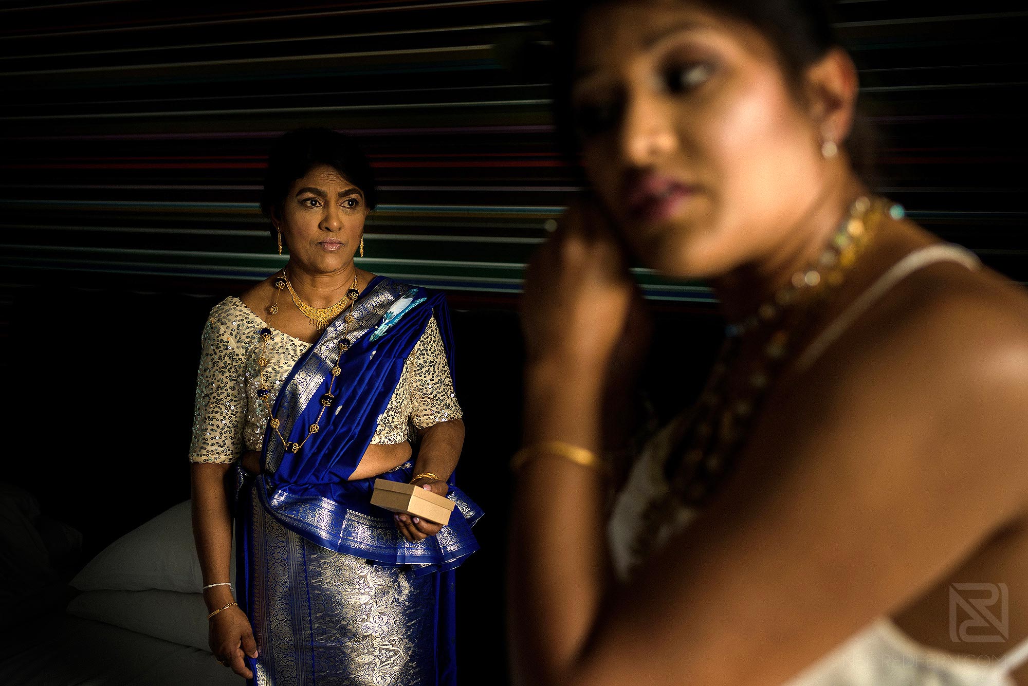 mother of bride watching daughter put on wedding dress