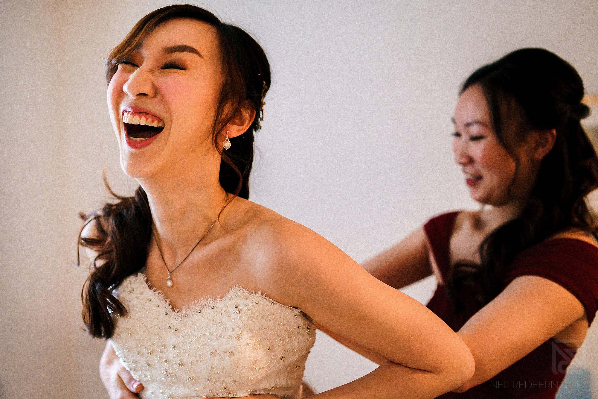 bride laughing putting on wedding dress