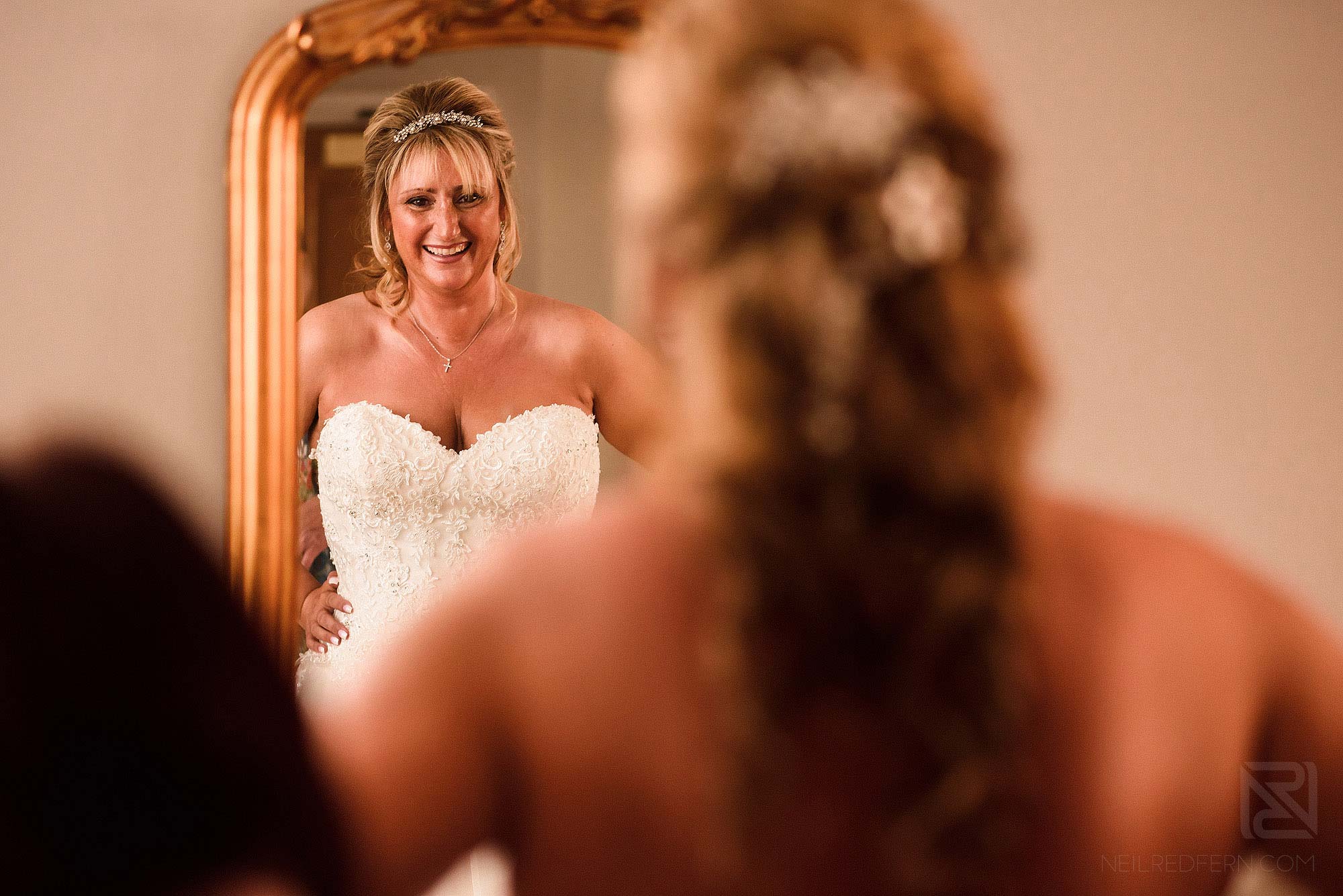 smiling bride looking in to mirror putting on wedding dress